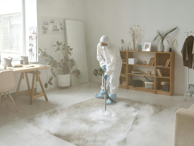 A person in protective gear disinfects a room with smoke, ensuring safety against germs.